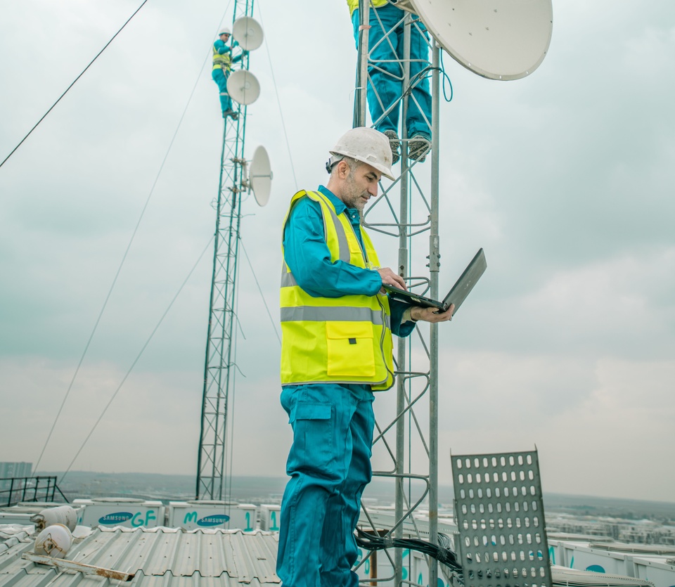 A field engineer checks a laptop at the base of a telecom mast